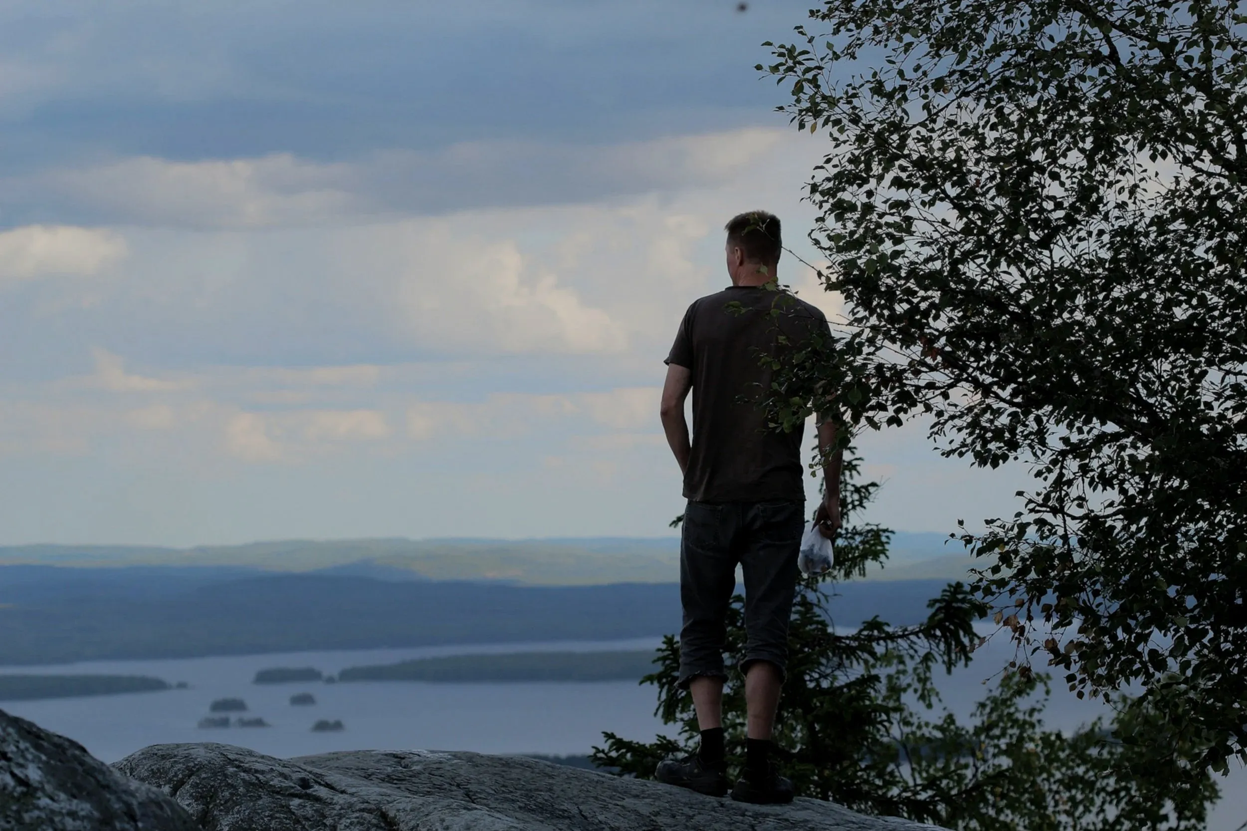 A man standing on a rocky overlook above a mountain lake at dusk